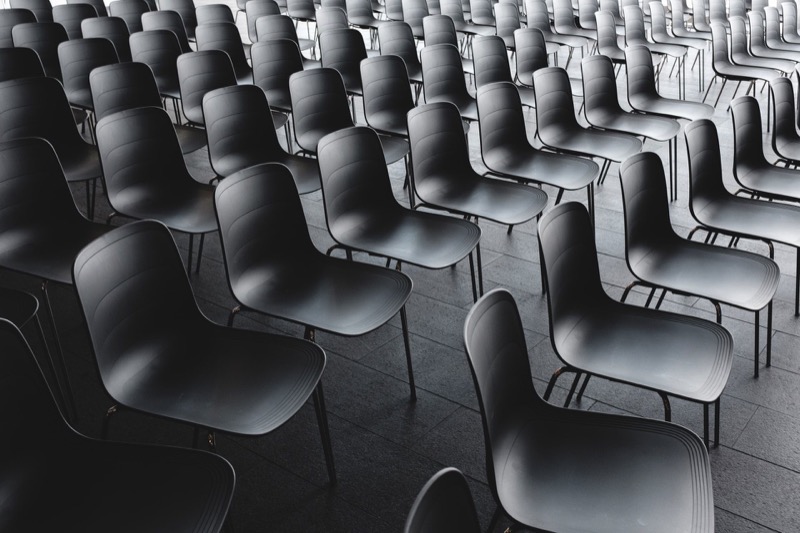 Reihen von leeren, dunklen Stühlen in einem Konferenz- oder Veranstaltungsraum mit grauem Boden.