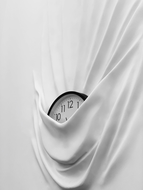 Schwarz-weiße Uhr, teilweise verdeckt von fließendem weißen Stoff.